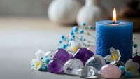 Healing crystals and gemstones arranged around burning blue candle for meditation, spiritual wellness and energy cleansing ritual practices.