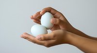Hands holding two white eggs against neutral background, suitable for food, nutrition, cooking, and wellness design projects.