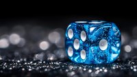 Translucent blue dice with white dots on sparkling dark surface, macro photography capturing glitter and bokeh effects in dramatic lighting setup.
