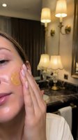 Young woman applying golden facial serum in luxury bathroom spa setting with elegant lighting for skincare routine and beauty treatment.