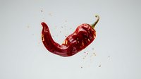 Red chili pepper with dynamic liquid splash and particles isolated on white background, suitable for food packaging, culinary design, and beverage marketing materials.