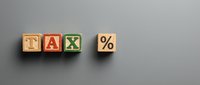 Wooden blocks spelling TAX with percentage symbol on gray background, representing taxation, financial planning, accounting, and business compliance concepts.
