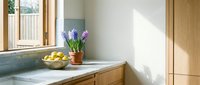 Modern kitchen interior with wooden cabinets, white countertop, purple hyacinth flowers in terracotta pot and fresh lemons in bowl creating warm homely atmosphere.