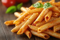 Cooked penne pasta with tomato sauce and fresh basil leaves on rustic wooden table, macro shot with selective focus showing texture and details of Italian cuisine.