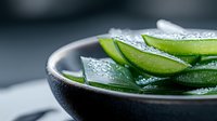 Fresh cucumber slices with water drops in dark ceramic bowl on gray background, macro food photography for healthy eating and spa concepts.