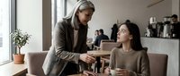 Two professional businesswomen shaking hands in modern office cafe during meeting. Corporate partnership, deal agreement, collaboration concept.