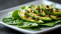 Fresh spinach salad with sliced avocado, mushrooms and herbs on white plate. Healthy vegan lunch with green vegetables and seasonings. Close up food photography.
