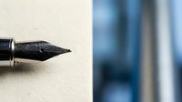 Fountain pen nib with black ink on textured cream paper, suitable for writing, calligraphy, stationery design, and educational content.