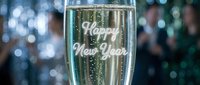 Champagne flute with Happy New Year text, sparkling bubbles, festive blurred party background with people celebrating the holiday.