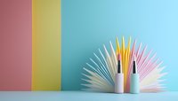 Minimalist composition with white paper fan and cosmetic bottles against colorful striped background, creating modern aesthetic for beauty and skincare marketing.