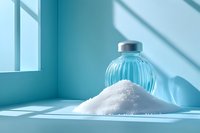 Pile of white salt crystals and vintage glass bottle in turquoise blue minimalist setting with dramatic window shadows creating modern composition.
