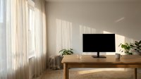 Modern minimalist home office workspace with wooden desk, computer monitor and houseplants by sunny window with sheer curtains for remote work productivity.