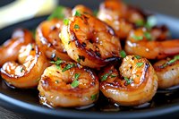 Grilled shrimp glazed with sweet and savory Asian sauce garnished with fresh herbs on black plate, close up view showing juicy texture and caramelized surface.