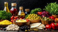 Mediterranean cuisine ingredients with fresh vegetables, legumes, olives, oils, and pita bread arranged on dark rustic background for healthy eating concept.