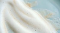 Creamy vanilla soft serve ice cream swirl with speckled texture against pastel blue background for dessert and food service marketing materials.