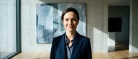 Confident female professional in dark blazer standing in modern office corridor with natural light, suitable for corporate, business, and leadership concepts.