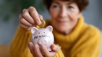 Mature woman in yellow sweater putting gold coin into pink ceramic piggy bank labeled pension, planning for retirement savings and financial security.