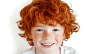 Portrait of happy redhead boy with curly hair and freckles smiling at camera on white background isolated for design use.