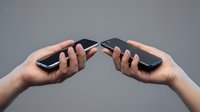 Two hands holding modern smartphones facing each other for data transfer, communication or file sharing on neutral background.