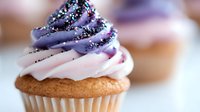 Purple and pink swirled frosting cupcake with colorful sprinkles on golden cake base, perfect for bakery displays and dessert marketing materials.