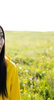 Young woman with long black hair and South Asian ethnicity wearing a bright yellow jacket, standing in a blooming wildflower meadow with colorful spring flowers and green grass.