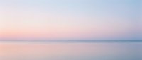 Serene dawn seascape with calm waters reflecting soft pastel sky in shades of pink, purple, and blue, evoking tranquility and peaceful morning atmosphere for wellness and nature projects.