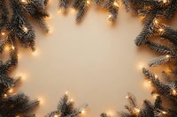 Glowing Christmas lights and pine branches create festive frame border on beige background, copy space for seasonal holiday greeting cards and designs.
