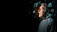 Middle-aged Caucasian man looking up at glowing digital icons representing technology, innovation and future concepts on dark background.