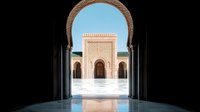 Ornate archway framing view of traditional Moroccan architecture with decorative facade and courtyard in bright sunlight against blue sky.