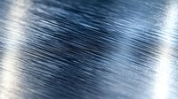 Brushed metal surface with diagonal lines creating dynamic texture and reflective sheen in blue and silver tones, suitable for industrial and tech backgrounds.