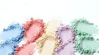 Colorful makeup powder swatches in pastel rainbow shades scattered on white background for cosmetic and beauty product design applications.