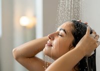 Young woman enjoying refreshing shower with water streaming over face and hair in modern bathroom for wellness and self-care routine.