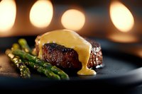 Juicy grilled beef tenderloin with creamy bearnaise sauce and fresh asparagus on black plate, soft bokeh lights in background create romantic atmosphere.