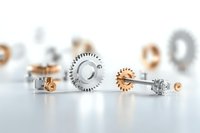 Metallic gears and mechanical parts in silver and copper colors arranged on white background, shallow depth of field creating artistic industrial composition.