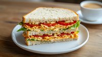 Fresh club sandwich with crispy bacon, lettuce, tomato and chicken on white bread, served on ceramic plate with coffee cup on wooden table background.
