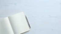Open notebook with blank dotted pages and gray pen on white wooden surface, ready for writing and planning.