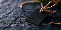 Black blank price tag with twine rope on dark stone background, minimalist retail mockup for branding and product pricing presentation.