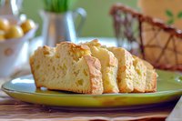 Freshly baked homemade pound cake slices on green ceramic plate, showing moist, golden crumb texture with natural lighting and soft background.