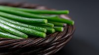 Fresh green onion stalks arranged on dark woven basket against black background, macro food photography with selective focus and natural lighting.