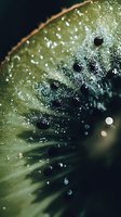 Fresh kiwi slice macro with water drops and seeds in dramatic lighting, showing juicy green flesh texture and natural organic patterns.