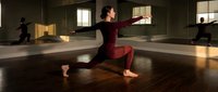 Woman in burgundy athletic wear performing low lunge yoga pose in modern studio with mirrors and natural light, suitable for fitness, wellness and exercise content.
