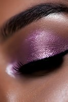 Close-up of eye makeup featuring shimmering purple eyeshadow and dramatic black eyeliner on dark skin, showcasing professional beauty and cosmetic application technique.