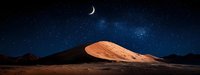 Panoramic desert landscape at night with crescent moon illuminating golden sand dune against starry sky and mountains, dramatic natural scenery.