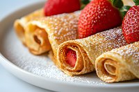 Fresh strawberry crepes dusted with powdered sugar on white plate, rolled French-style thin pancakes filled with red berries, close up view of sweet dessert.
