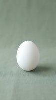 Single white chicken egg standing upright on soft green linen fabric background with natural lighting and minimalist composition for cooking and food concepts.