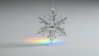 Crystal snowflake ornament casting rainbow light spectrum on white surface creating prismatic effect for holiday decoration and winter celebration.