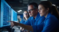 Professional team analyzing data on multiple screens in dark office environment, pointing at code displays while collaborating on cybersecurity project.
