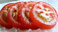 Fresh ripe tomato slices arranged in row showing juicy flesh and seeds, macro photography with soft natural lighting on white background.