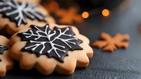 Festive snowflake cookies decorated with black and white royal icing on dark background with bokeh lights. Holiday baking and winter celebration treats.