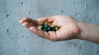 Caucasian hand holding green and yellow capsule supplements against textured concrete wall background for healthcare and wellness design use.